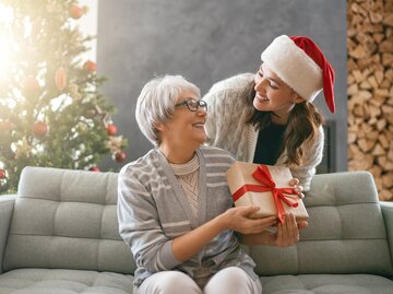 Eine junge Frau mit Weihnachtsmütze gibt ihrer Mama ein Weihnachtsgeschenk | © GettyImages/Choreograph