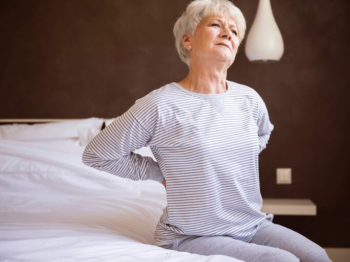 Reife Frau hält sich Rücken vor Schmerzen | © Getty Images/gpointstudio