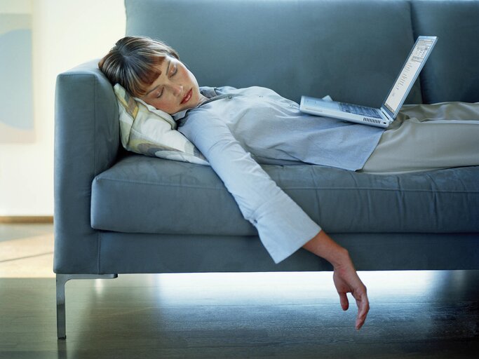 Frau ist mit ihrem Laptop auf dem Schoss auf der Couch eingeschlafen | © Getty Images/Daly and Newton