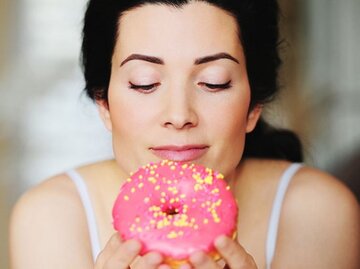 Dunkelhaarige Frau starrt auf einen rosafarbenen Donut. | © EmmaKStudio, Getty Images