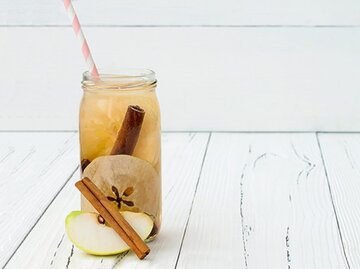 Ein Glas Apfel-Zimt-Wasser steht auf einem weißen Holztisch. | © sveta_zarzamora, Getty Images