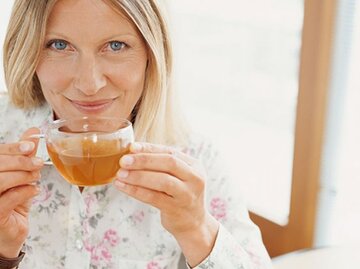 Blonde Dame trinkt lächelnd aus einer Glastasse Tee. | © David Lees, Getty Images