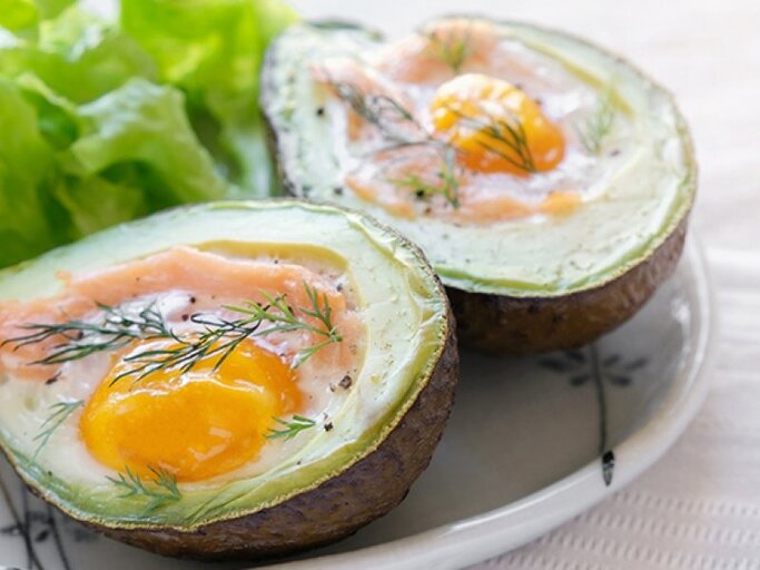 Aufgeschnittene Avocado-Hälften gefüllt mit einem Ei und Lachs auch einem Teller. | © ThitareeSarmkasat, Getty Images