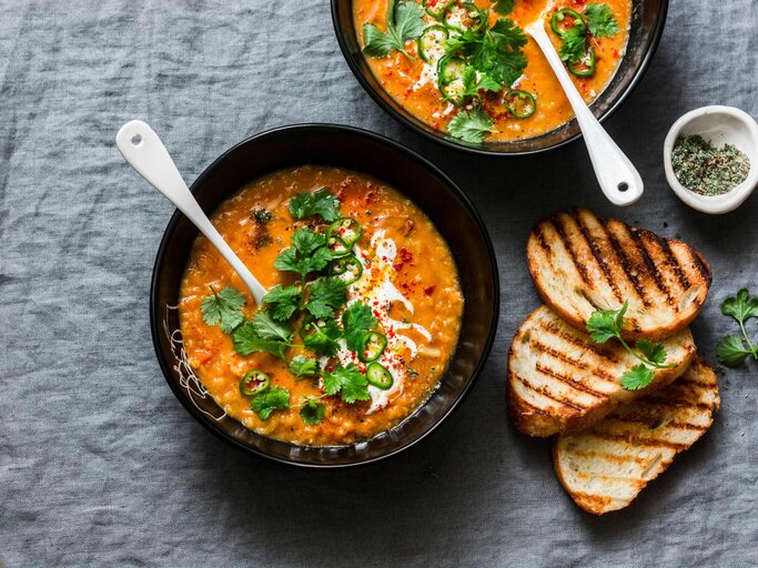 Curry rote Linsen Tomate und Kokos-Suppe - leckere vegetarische Kost auf grauem Hintergrund, Ansicht von oben. Flache Lay gesundes Mittagessen serviert  | © Getty Images/OksanaKiian