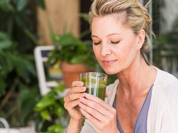 Reife Frau trinkt einen Smoothie mit Gerstengras und ist entspannt | © Getty Images / Westend61