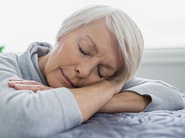 Ältere Dame legt schlafend ihren Kopf auf ihren verschränkten Armen ab. | © Hero Images, Getty Images