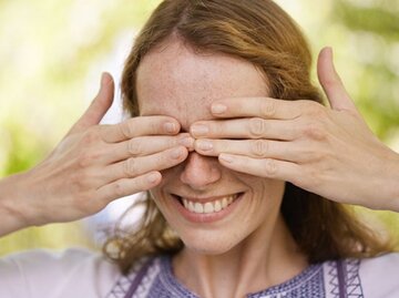 Lächelnde Frau im Garten hält sich mit de Händen die Augen zu. | © Cultura RM Exclusive/Stephen Lux, Getty Images