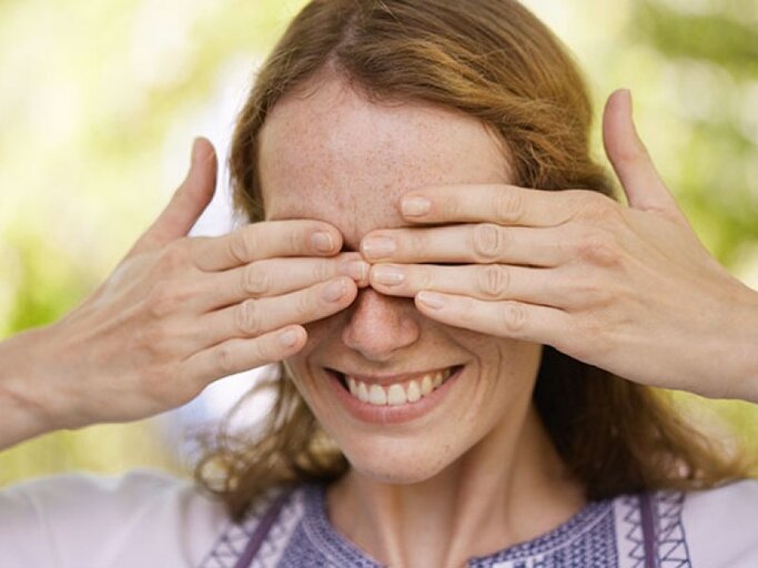 Lächelnde Frau im Garten hält sich mit de Händen die Augen zu. | © Cultura RM Exclusive/Stephen Lux, Getty Images