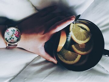 Eine Hand mit Uhr hält eine Tasse mit Zitronen und Orangenscheiben. | © Abby Kihano, stocksnap.io