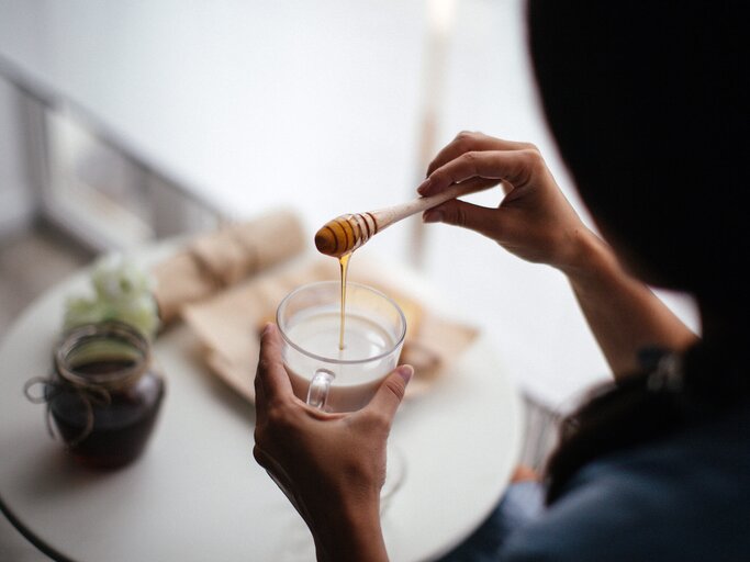 Frau gibt Honig in ein Glas warme Milch | © gettyimages.de | StefaNikolic