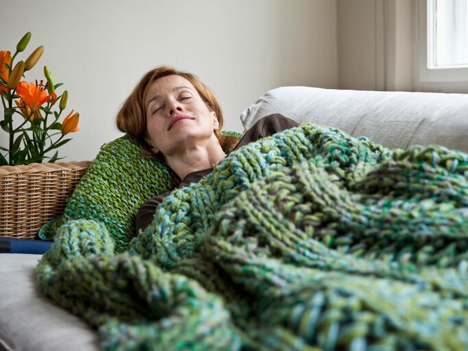 Frau liegt mit Lächeln und Kopfkissen auf der Couch | © gettyimages.de | Halfdark