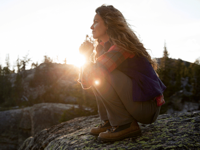 Frau sitzt auf Felsen bei Sonnenuntergang  | © Jordan Siemens, Getty Images