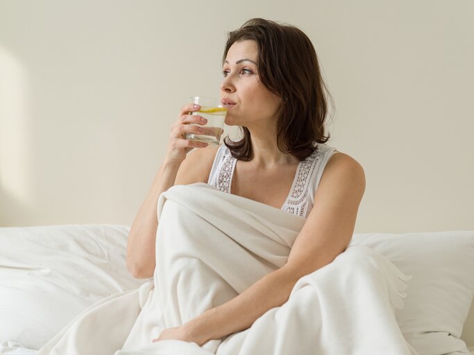 Frau sitzt im bett und trinkt Wasser. | © istock; Valeriy_G