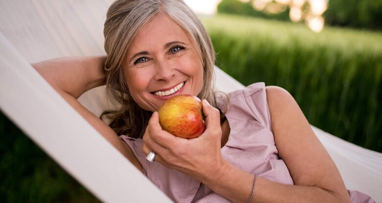 Hübsche Frau, mittleren Alters isst einen Apfel in der Hängematte | © iStock | wundervisuals