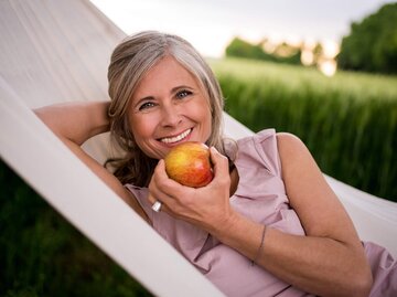 Hübsche Frau, mittleren Alters isst einen Apfel in der Hängematte | © iStock | wundervisuals