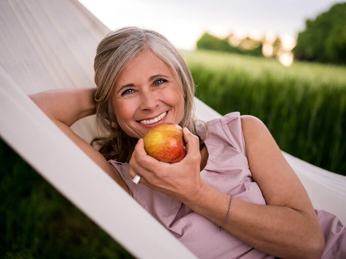 Hübsche Frau, mittleren Alters isst einen Apfel in der Hängematte | © iStock | wundervisuals