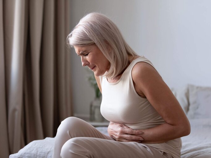 Ältere Frau sitzt auf dem Bett und leidet unter starken Schmerzen Bauchschmerzen. | © iStock | fizkes