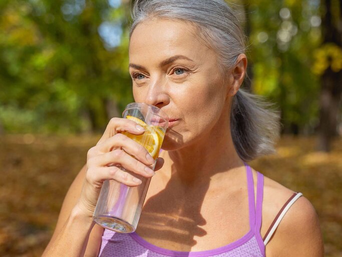 Reife Frau trinkt aus einer Sportflasche Wasser | © iStock | yacobchuk