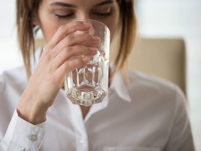 Frau mit weißer Bluse trinkt ein Glas stilles Wasser. | © iStock | fizkes