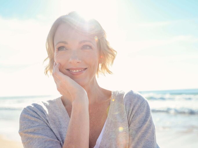 Hübsche Frau am Strand blickt in die Sonne | © iStock | courtneyk