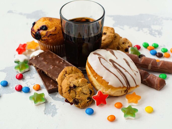 Produkte mit viel Zucker auf einem Haufen: Kekse, Gummibärchen, Kuchen und Cola | © iStock | happy_lark