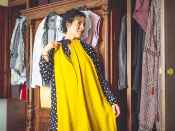 Frau mistet ihren Kleiderschrank aus und hält ein gelbes Kleid in der Hand.  | © iStock | Eva-Katalin