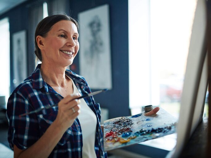 Frau steht vor einer Staffelei und malt ein Bild. | © iSock | shironosov