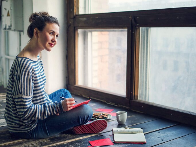 Frau sitzt auf dem Boden und schreibt viele kleine Briefe und Notizen. | © iStock | Alexandra Iakovleva