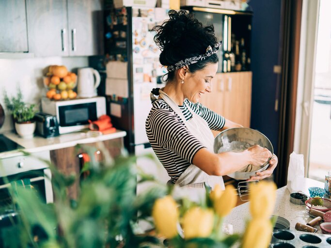 Frau mit schwarzen Locken steht in der Küche und backt Muffins. | © iStock | Vladimir Vladimirov