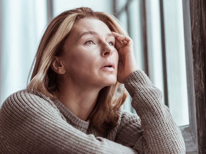 Frau sitzt am Fenster und hält sich den Kopf. | © iStock | Zinkevych