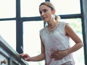 Frau steht auf der Treppe und hat Magen-Darm-Schmerzen. | © iStock | yacobchuk