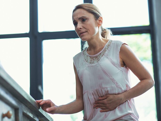 Frau steht auf der Treppe und hat Magen-Darm-Schmerzen. | © iStock | yacobchuk