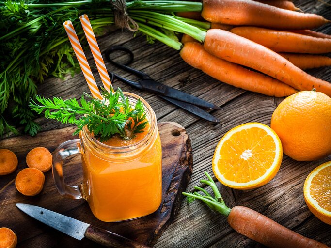 Rustikaler Holztisch mit aufgeschnittenen Orangen, frischen Karotten und einem Glas mit frischgepresstem Saft. | © iStock | fcafotodigital