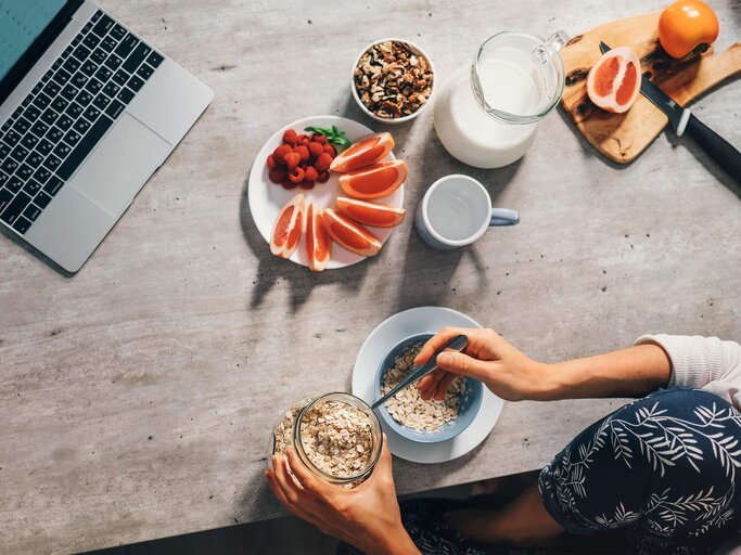Frau sitzt am Tisch mit Laptop und frühstückt Haferflocken. | © iStock | Solovyova