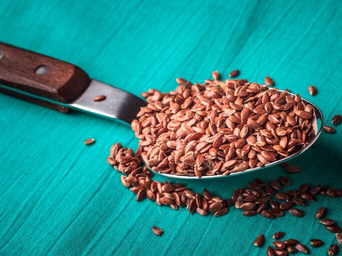 Löffel gehäuft mit Leinsamen liegt auf einem blauen Holztisch. | © iStock.com / Anetlanda