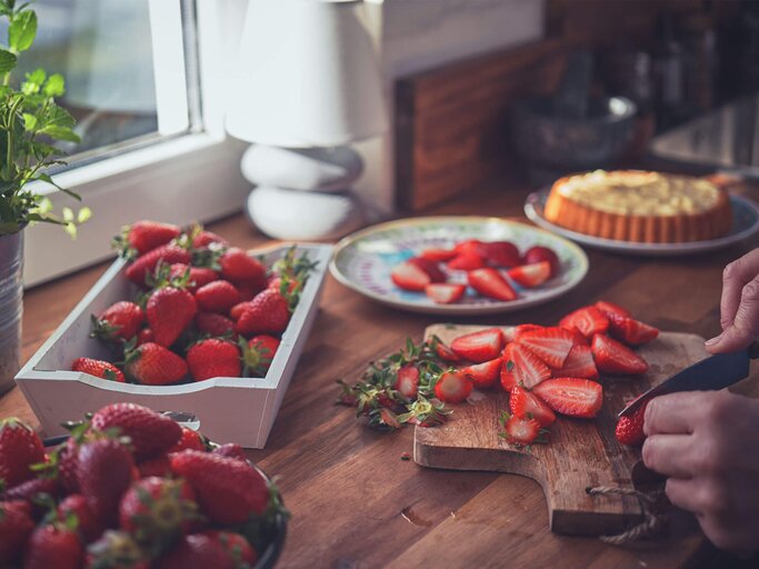 Frau schneidet frische Erdbeeren in der Küche und bereitet einen Kuchen vor.  | © iStock.com / GMVozd