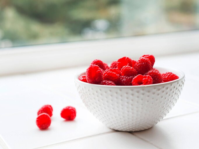 Portion Himbeeren in einer weißen Schüssel, die am Fenster steht. | © iStock.com / ballycroy