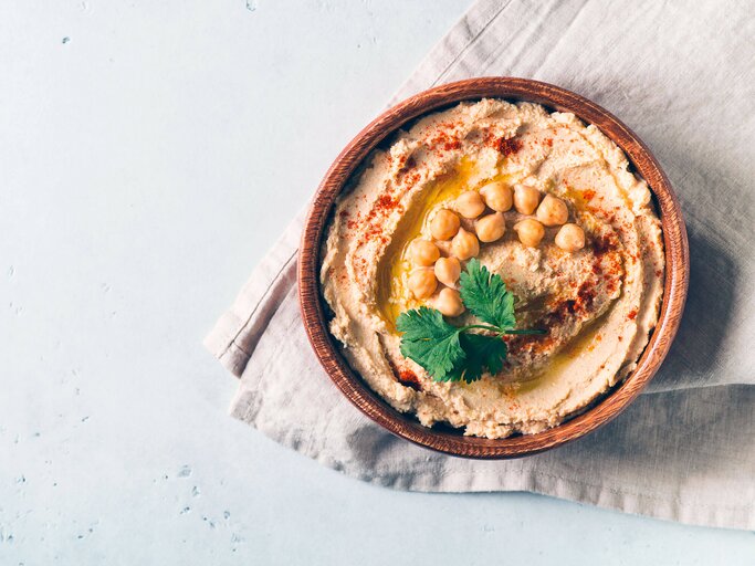 Hummus Dip mit Kichererbsen und Petersilie in Holzplatte auf einem weißen Tisch. | © iStock.com / Dannko