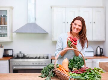 Frau steht in der Küche und hält einen Bund Radieschen. | © iStock.com / STEEX