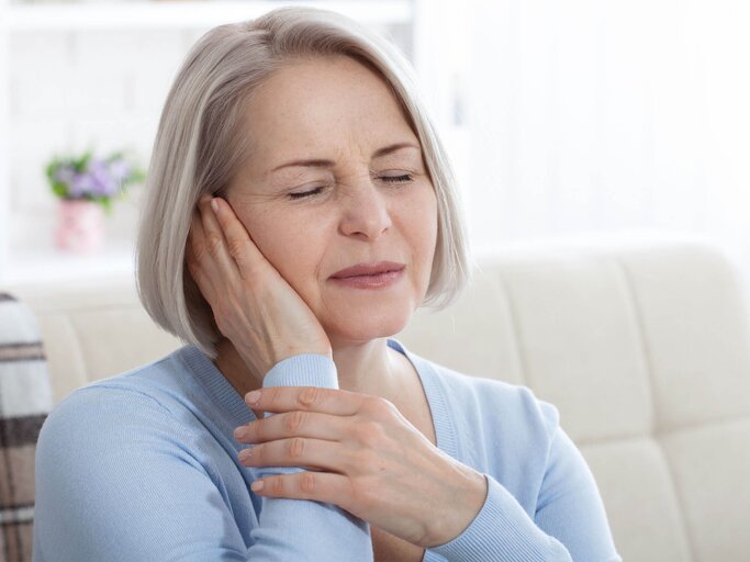 Frau hält sich eine Hand an die Schläfen, weil sie Ohrenschmerzen hat. | © iStock.de / Victor_69
