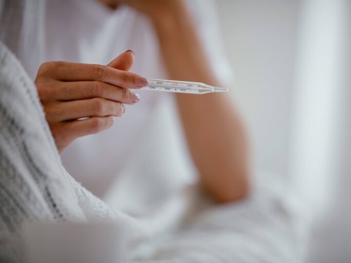 Frau hält ein Fieberthermometer in der Hand.  | © iStock.com / Milos Dimic