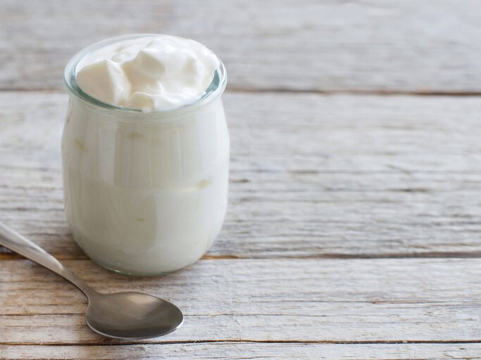 Ein Glas gefüllt mit Joghurt auf einem rustikalen Holztisch | © iStock.com / Karisssa