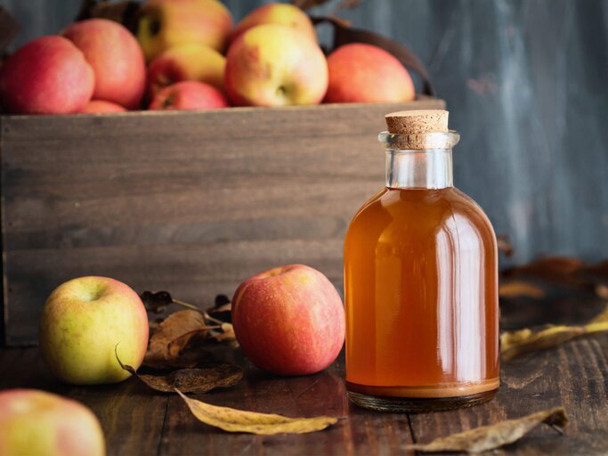 Apfelessig in einer Glasflasche mit frischen Äpfeln in einer Holzkiste. | © iStock.com / StephanieFrey