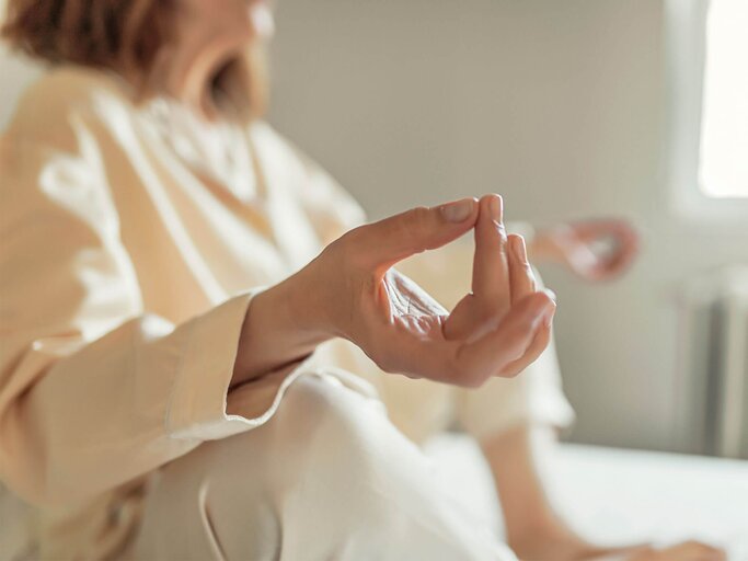 Frau sitzt entspannt auf dem Boden und meditiert. | © iStock.com / PixelsEffect