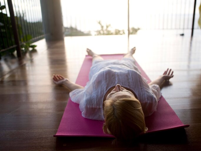 Frau liegt entspannt auf dem Rücken auf einer Yoga-Matte. | © iStock.com / webphotographeer