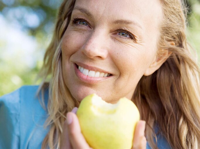 Frau ist an der frischen Luft und isst einen Apfel. | © gettyimages.de / Soren Hald