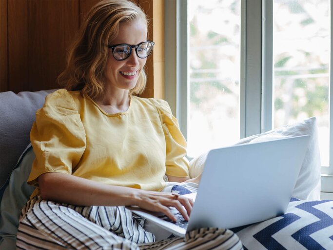 Frau sitzt am Fenster mit ihrem Laptop. | © iStock.com / Jovana Simovski