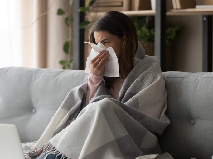 Frau sitzt mit Decke auf der Couch und hat eine Erkältung. | © iStock.com / fizkes