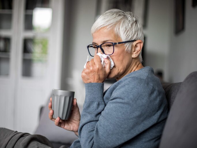 Reife Frau mit Brille putzt sich die Nase | © gettyimages.de | Nikola Ilic