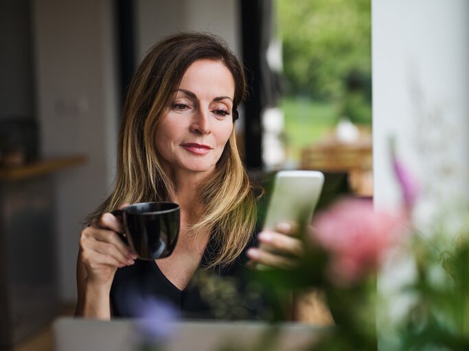 Frau trinkt einen Kaffee und blickt auf ihr Smartphone | © gettyimages.de /  Halfpoint Images